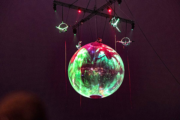 Photo of performers suspended from a crane around an inflated sphere.